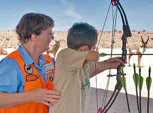 Become a Wildlife Conservation Volunteer. (Photo of archery instructor helping youth). New Mexico Department of Game and Fish